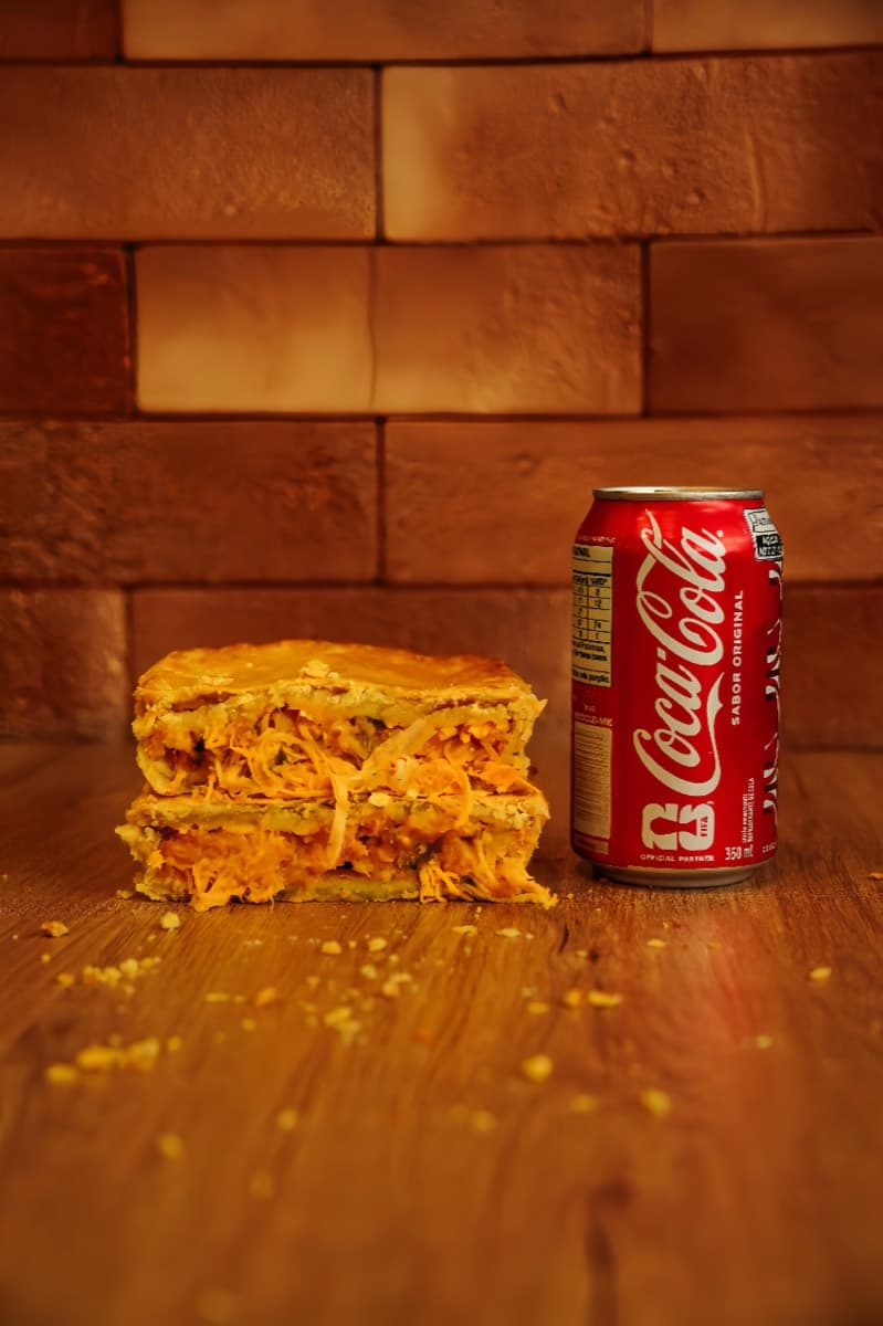 Empada de frango cortada ao meio, recheio até a borda, ao lado de uma lata pra dar a escala