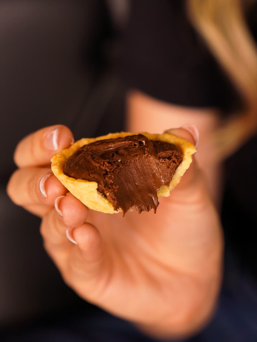 Mão segurando uma empada de chocolate aberta, com o recheio à mostra